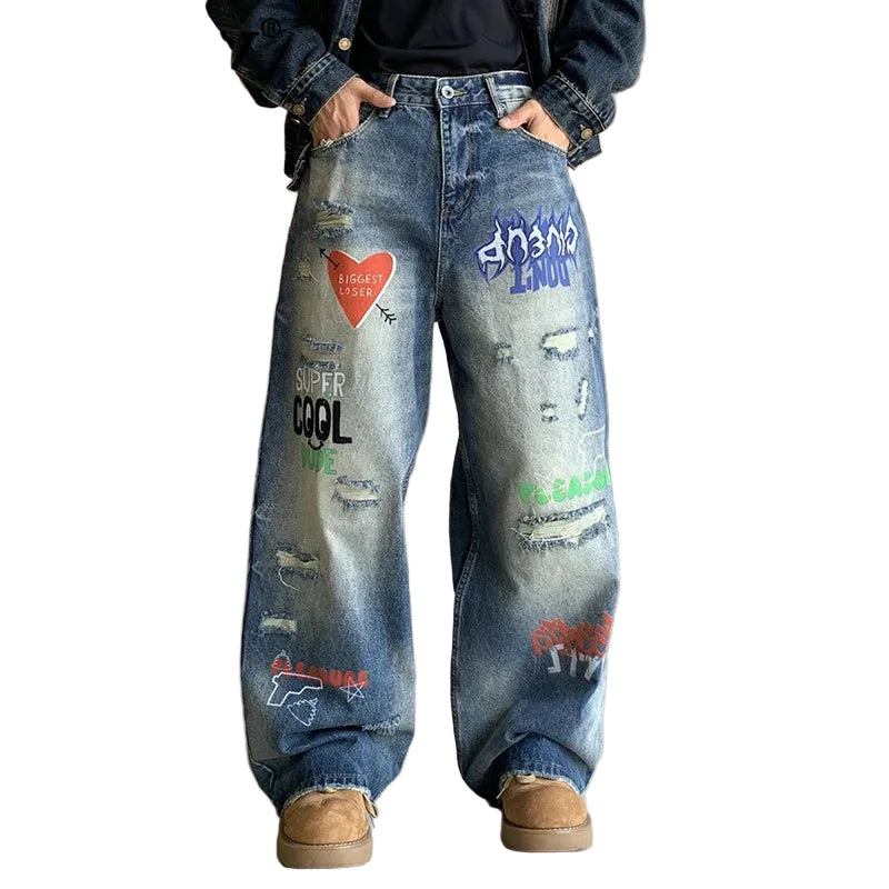 Person wearing blue jeans with graffiti-style text and designs, standing indoors.